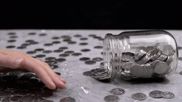 Female Hand Counting the Scattered Coins on the Table from an Inverted Glass Jar. A lot of pennies on a gray concrete background. Financial crisis, budget, savings, money accumulation. Cash. Poverty.