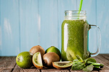 Front view of blended green smoothie with kiwi, lime and mint isolated on blue wooden background 