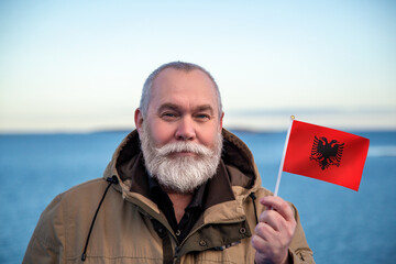 Man holding Albania flag. Portrait of older man with a national Albanian flag. Visit Albania. Older man 50 55 60 years old with gray beard outdoors travelling in winter. Travel to Albania. - 560508531