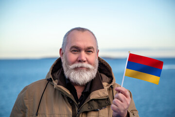 Man holding Armenia flag. Portrait of older man with a national Armenian flag. Visit Armenia concept. Older man 50 55 60 years old with gray beard outdoors travelling in winter. Travel to Armenia - 560508561