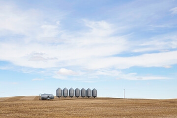 A row of steel grain bins with two toppled over in a harvested field in an autumn agricultural landscape