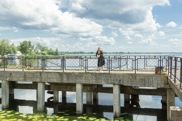 beautiful girl in a black dress on the background of the river, sea with blue sky and clouds