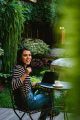 young woman drinking coffee and working at a table while having breakfast