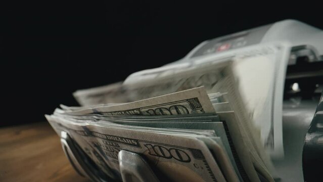 Close-up side view of a cash counting machine pushing out one hundred USD bills on the stacker