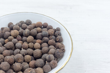 Allspice peas scattered in a white bowl on white wooden background