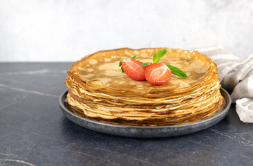 A stack of french crepes, pancakes or Russian bliny with strawberries on a gray background....