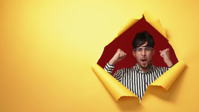 Winner yes. Success celebration. Victory triumph. Excited overjoyed satisfied man showing wow expression in orange breakthrough torn paper hole copy space background.