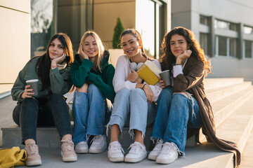 Front view of four college students sitting on the stairs of the college building