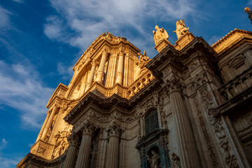 Detail of the monumental baroque facade of the cathedral of Murcia, Spain profusely decorated with sculptures and architectural details and creating a play of light and shadow at sunset