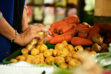 man's hands packing yellow creole potatoes in plastic bag in the middle of a fruit and vegetable market