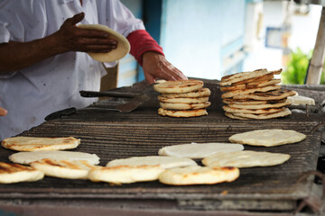 Woman's hands grilling Colombian arepas at a traditional stand in the streets of Colombia.