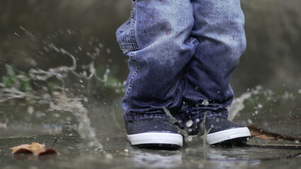 Toddler boy splashes into puddle of water. Child plays with puddles6