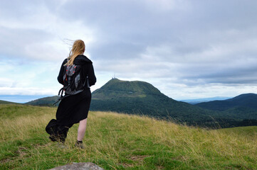 A women hiker on top of a mountain with a beautiful view of volcanic mountains. The Puy de Dome volcano is a unesco listed site.