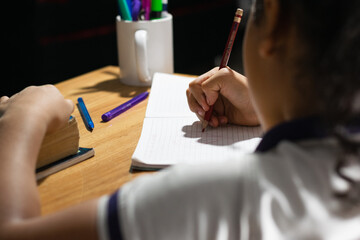 detailed view of a little latin girl's hands drawing on her notebook on top of a wooden desk. doing...