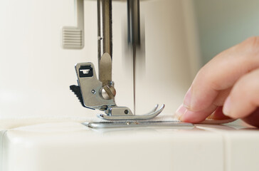 A female seamstress sews white fabric items on a sewing machine.