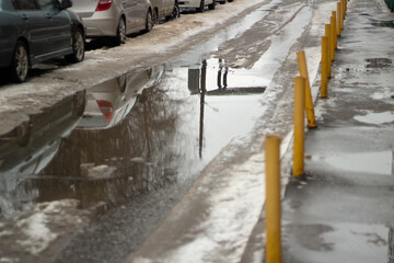 Puddle in road. Melted snow in city. Yellow parking limiters.