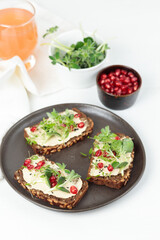 Sandwiches with soft cheese, microgreens, pomegranate seeds. Close-up on a white background, a glass of juice in the background.