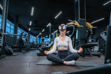 Young athletic woman in virtual reality headset practicing meditation in the gym.Wellness,relaxation,slow life. healthy meditation,Practicing Meditation - obrazy, fototapety, plakaty