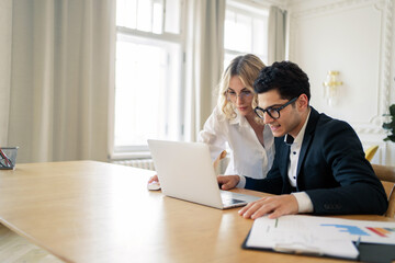 Colleagues are working in the office together on a new startup project. A man and a woman in business suits, brainstorming over plans for the next year. Office employees together around a laptop.