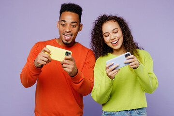 Young couple two friends family man woman of African American ethnicity wear casual clothes together use play racing app on mobile cell phone gadget isolated on pastel plain light purple background. © ViDi Studio