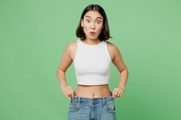 Young amazed surprised woman wear white clothes show loose pants on waist after weightloss isolated...