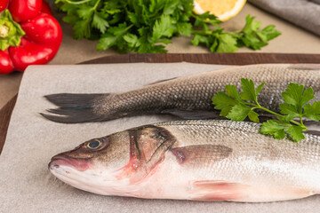 Fresh raw sea bass fish, lemon slices, parsley, red pepper  and salt on wooden table, closeup