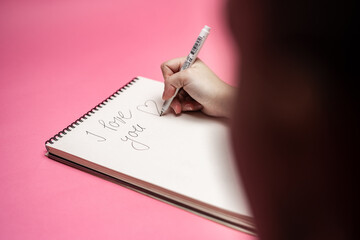 Person writing I love you note in a notebook. Valentine's day themed photo. 