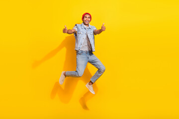 Fototapeta na wymiar Full length photo of cool cheerful guy dressed denim clothes jumping high showing thumbs up isolated yellow color background