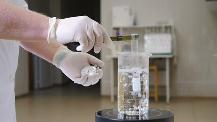 Laboratory research. Round glass flask with transparent liquid being heated. Chemical reaction. Sparkling solution in glass with bubbles. Reseacher holding test tube with chemicals and stopwatch. 4 k - Powered by Adobe