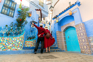 Colorful journey from Morocco. Young couple in red dress walking in the medina of the blue city...