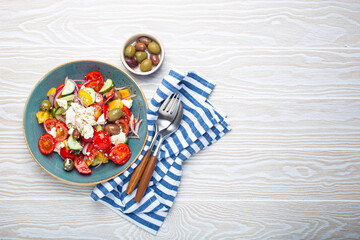 Greek fresh healthy colorful salad with feta cheese, vegetables, olives in blue bowl on rustic white wooden background top view, Mediterranean diet, traditional cuisine of Greece. Space for text