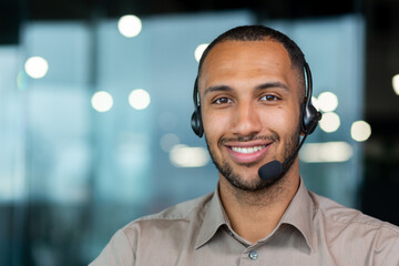 Close up hispanic male worker with video headset smiling and looking at camera, tech support worker...