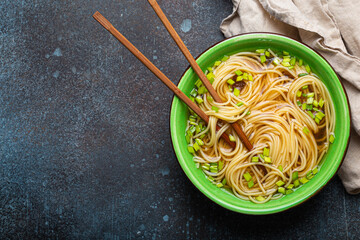 Asian noodles soup in green rustic ceramic bowl with wooden chopsticks top view on rustic stone...