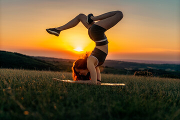 A beautiful red hair yoga teacher does yoga stand on his elbows outdoors in the hills. Sunset and hill layers in background.