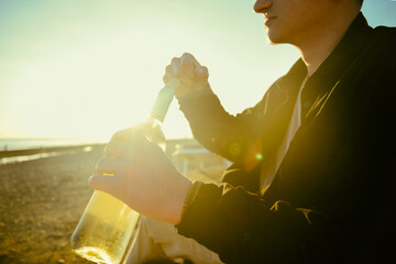 A man on the shore of the sea or ocean opens a bottle of white wine. A date on the beach, alcohol...