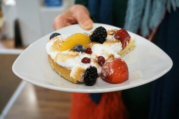 Frauenhand hält weißen Teller mit Stück Obstkuchen 