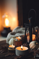 Cozy autumn composition with aromatic candle, pumpkins, wool sweater, leaves, cinnamon. Aromatherapy on a grey fall morning, home atmosphere of cosiness and relax. Wooden background close up.