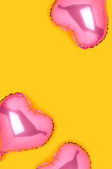 Pink inflatable foil balloons in a heart shape. Festive composition on a yellow background.