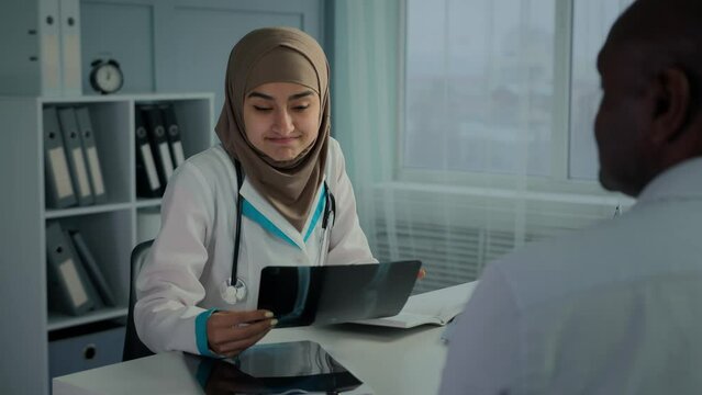 Female doctor woman in hijab neurologist radiologist analyze MRI scan x-ray diagnostic result make professional radiology expertise check trauma on image talk with male patient on medical consultation