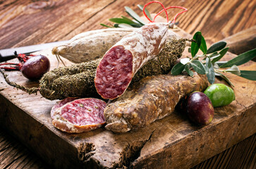 Traditional Italian salami with black ripe olives served as close-up on an old wooden cutting board