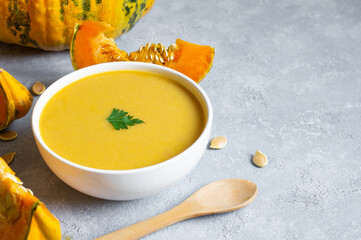 Homemade pumpkin carrot soup with parsley in bowl and fresh pumpkins on rustic background