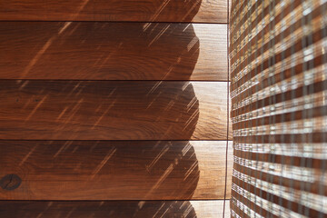 Detail of straw blinds dropping shadow lights on wooden wall of a log housу. Selective focus.