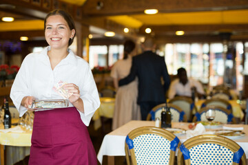 Cheerful young waitress received good tips standing with money in restaurant and smiling