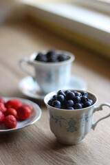 Vintage porcelain cups and plates filled with various fresh berries. Wooden background, selective focus.