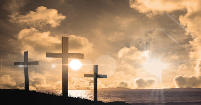 Image of three christian crosses over landscape with sun glowing on orange sky