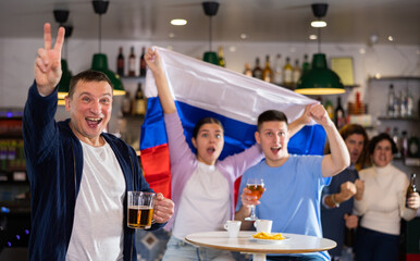 Company of joyful supporters waving flag of Russia and celebrating victory of football team in...