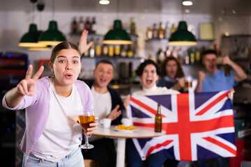 Company of joyful sports supporters waving flag of Great Britain and celebrating victory of favotite team in pub