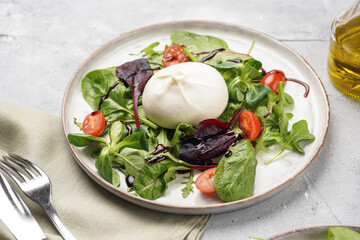 Plates with arugula and spinach salad with fresh cherry tomatoes and italian fresh cheese burrata with balsamic vinegar dressing on a light grey concrete background