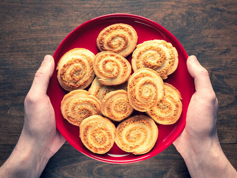Deliciously crisp flaky cookies in the shape of a spiral on a red plate in human hands. Homemade Arlette Biscuits, top view