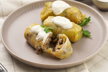 Three vegetarian cabbage rolls stuffed with rice, mushrooms, carrots and onions topped with vegan sour cream - traditional ukrainian dish during religious fasting time periods - on a grey plate